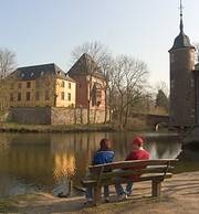 Zwei Menschen sitzen auf einer Bank und schauen auf Schloss Burgau