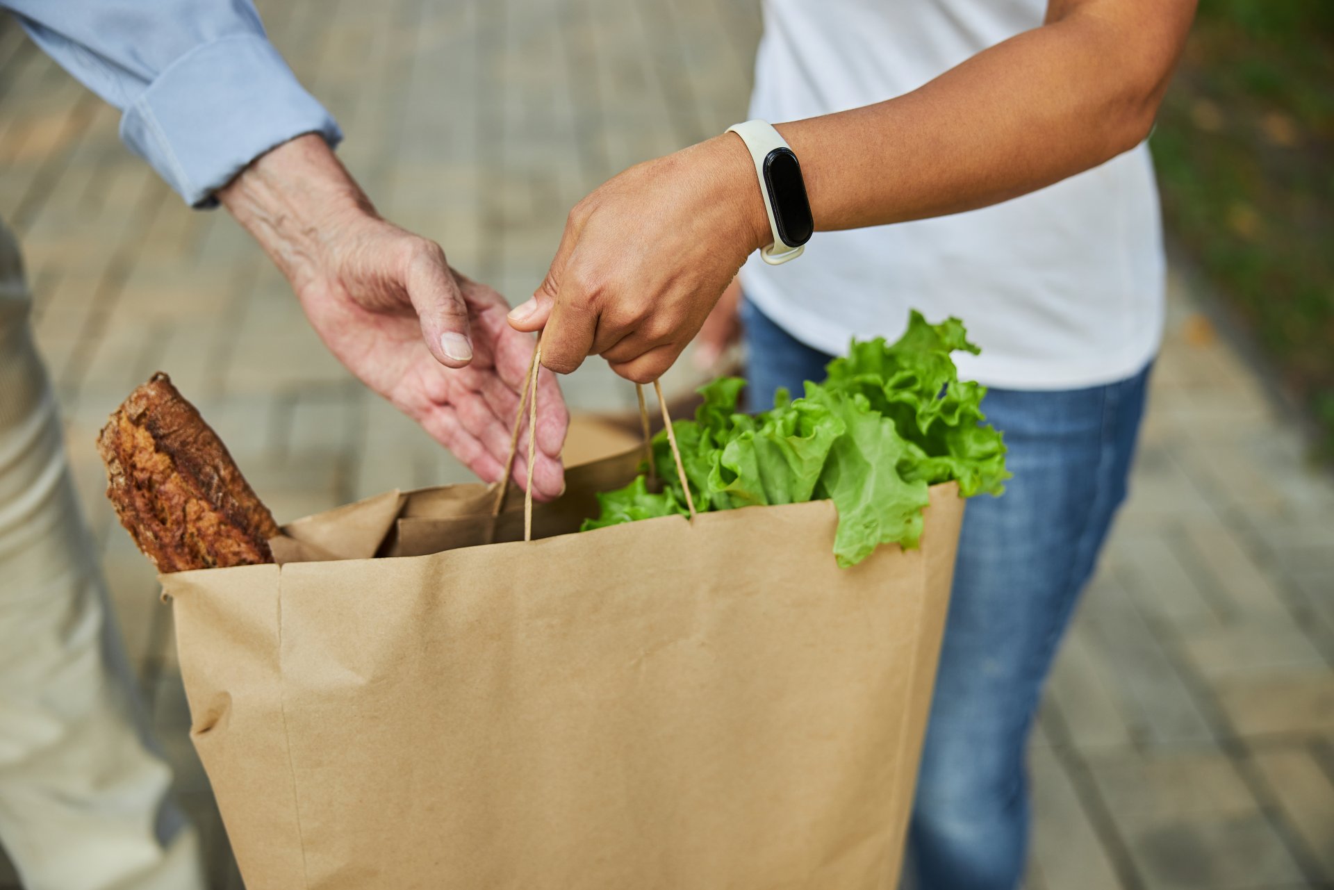 Das Bild zeigt, wie eine jüngere Person einer älteren Person eine Einkaufstasche übergibt